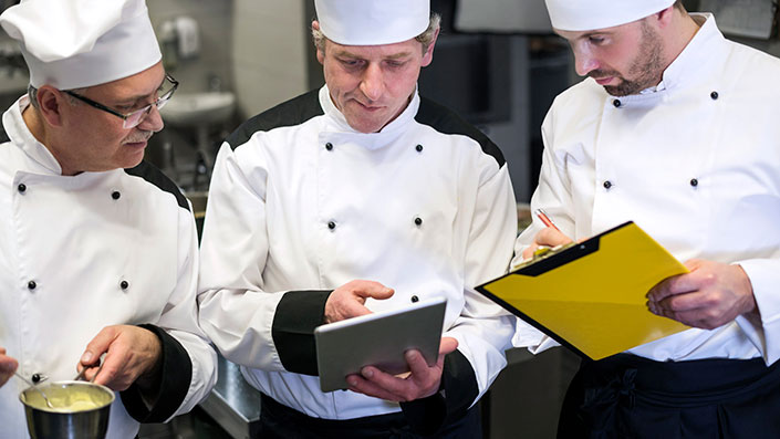 three food workers reviewing a tablet